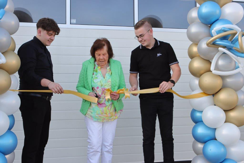 Opening nieuwe bedrijfspand uitgevoerd door moeder Ria Gubbels Janssen. Ze is 87 jaar en wordt geassisteerd door haar kleinzonen Bart en Gijs Gubbels